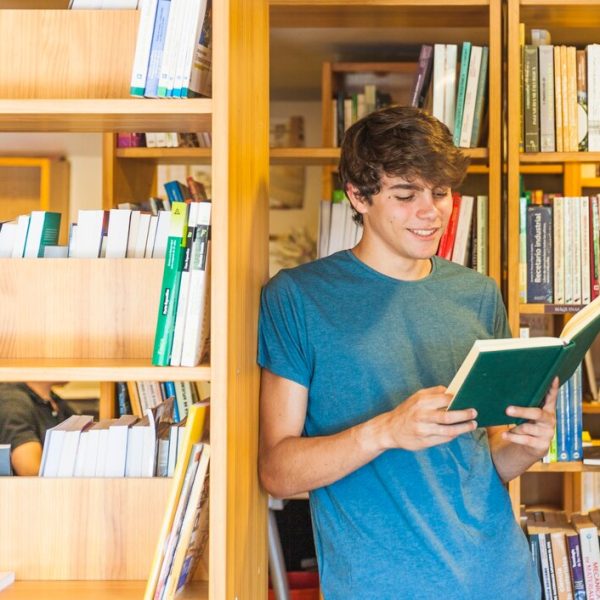 adolescente-sonriente-apoyandose-libreria-leyendo_23-2147864158